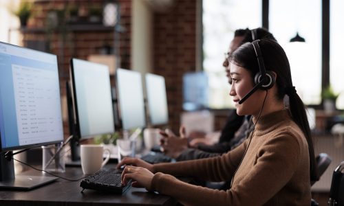 Paralyzed asian employee working at call center reception in disability friendly office. Female operator wheelchair user with impairment giving assistance on customer service helpline.